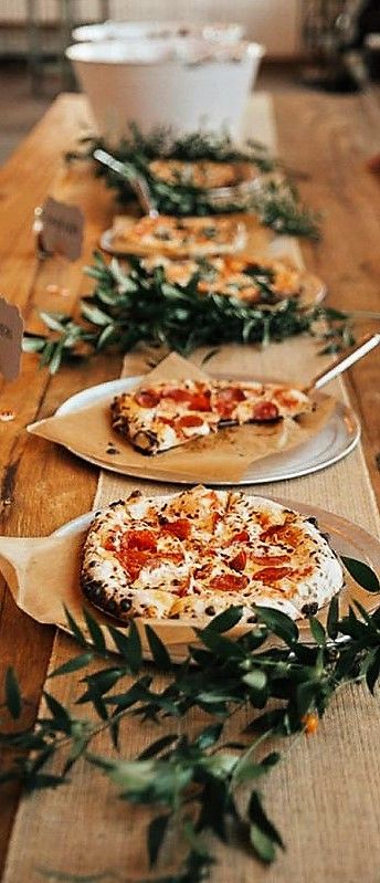 several pizzas on wooden trays lined up on a table with greenery around them