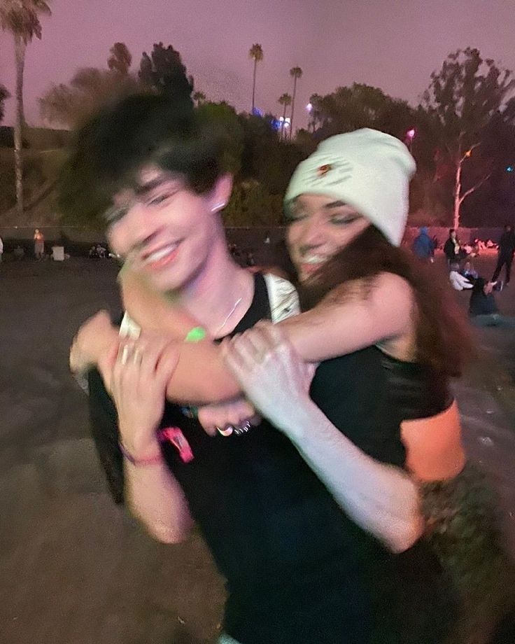 two young people hugging each other in the street at night with palm trees behind them