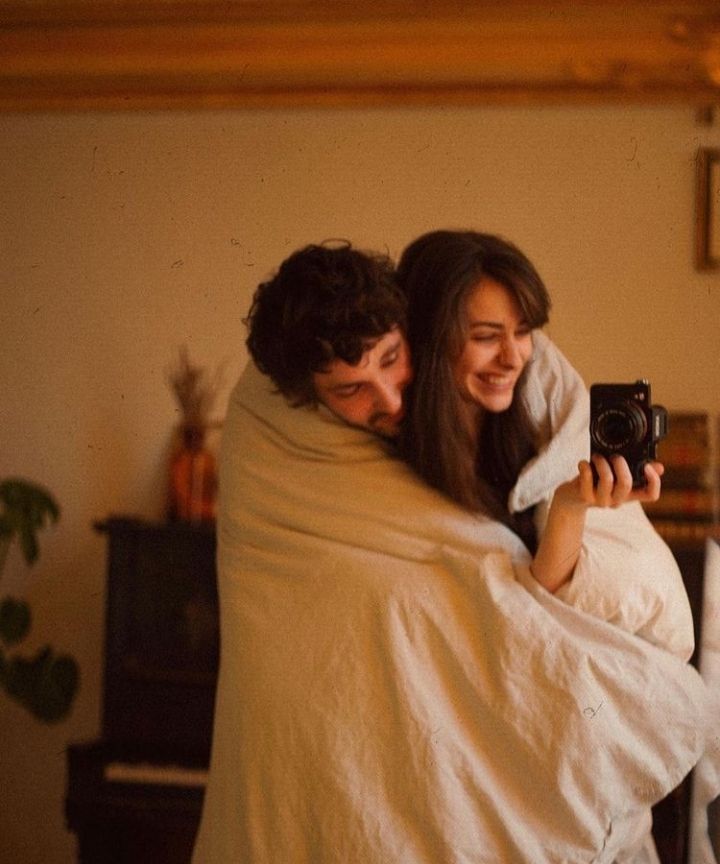 a man holding a woman wrapped in a blanket while she is taking a selfie