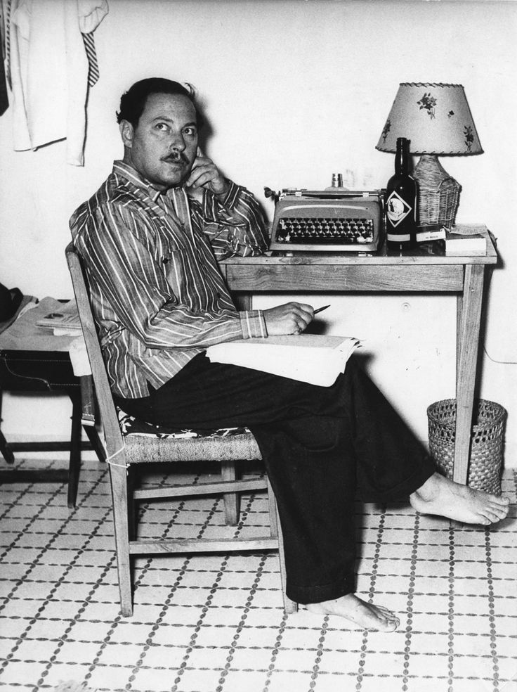 a man sitting at a desk with a typewriter and lamp on top of it