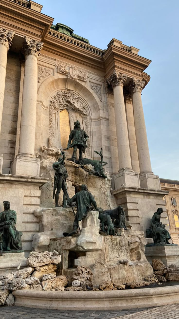 the fountain has statues on it and is in front of a large building with columns