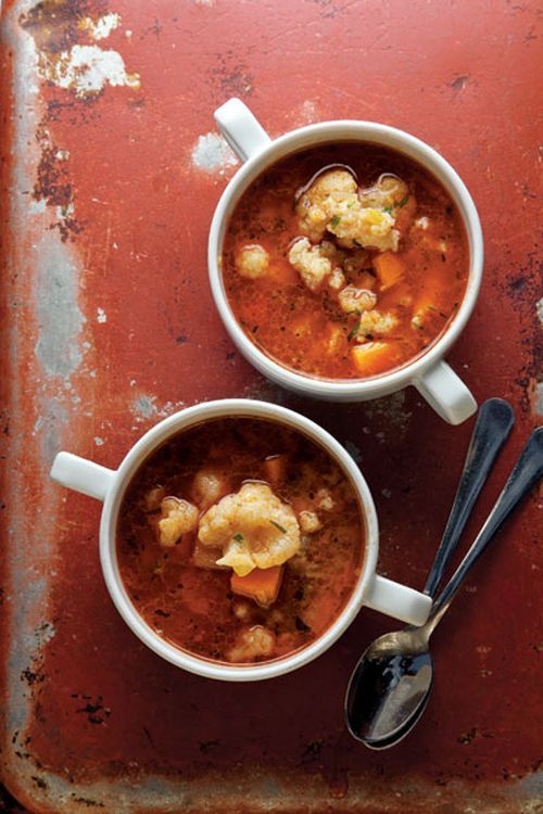 two white bowls filled with soup on top of a rusted metal tray next to spoons