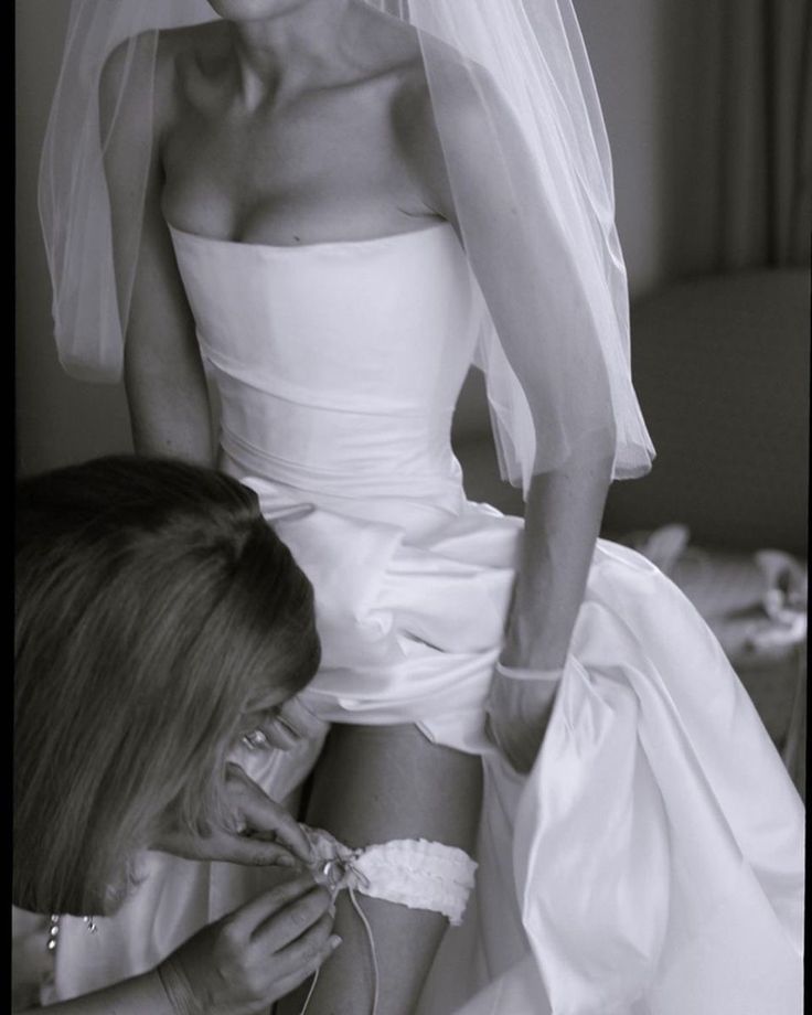 a woman in a wedding dress is fixing another woman's shoe