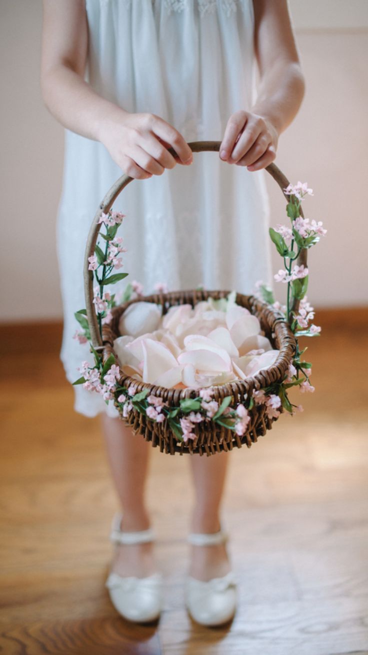 a woman is holding a basket with baby's shoes in it and flowers on the inside