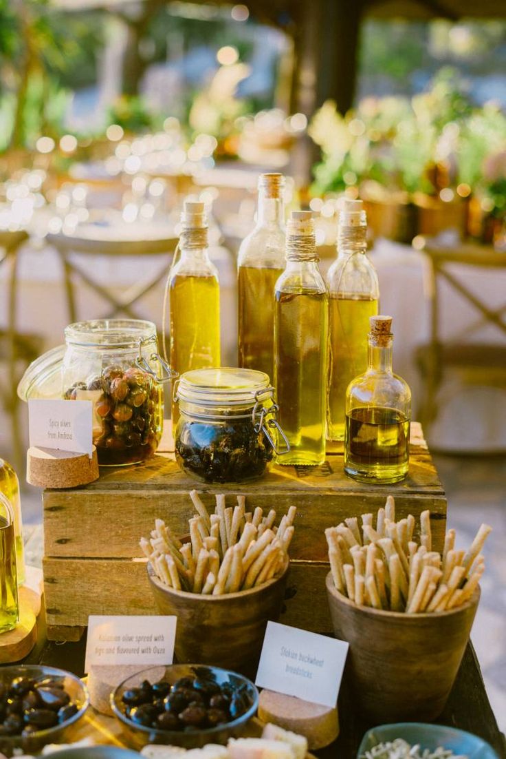 olives and other foods are on display at an outdoor wedding reception with bottles of olive oil