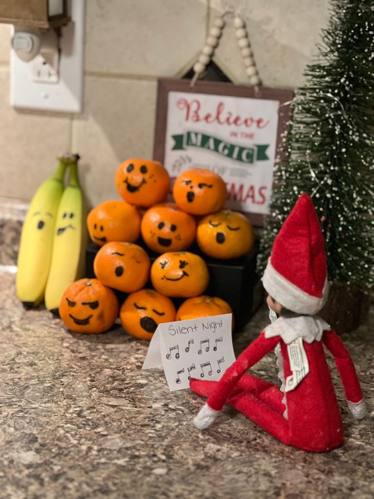 an elf is sitting on the counter next to some oranges and banana's