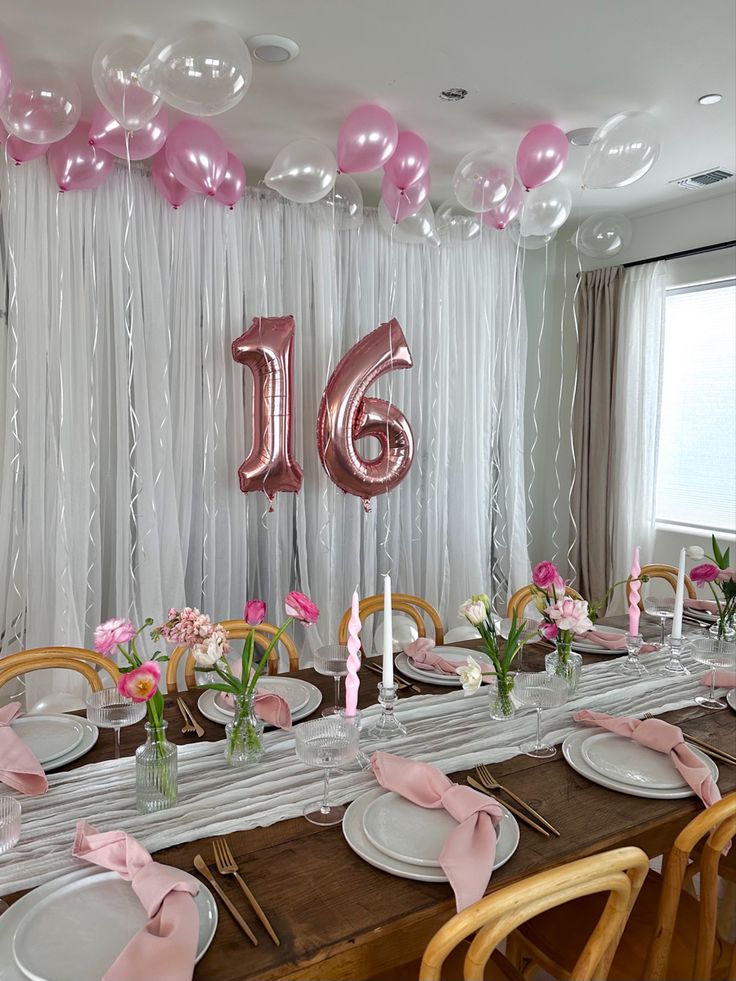 a long table with pink and white plates, silverware and balloons in the background