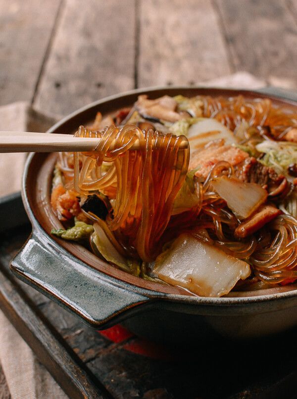 a wok filled with noodles and vegetables on top of a wooden table next to chopsticks