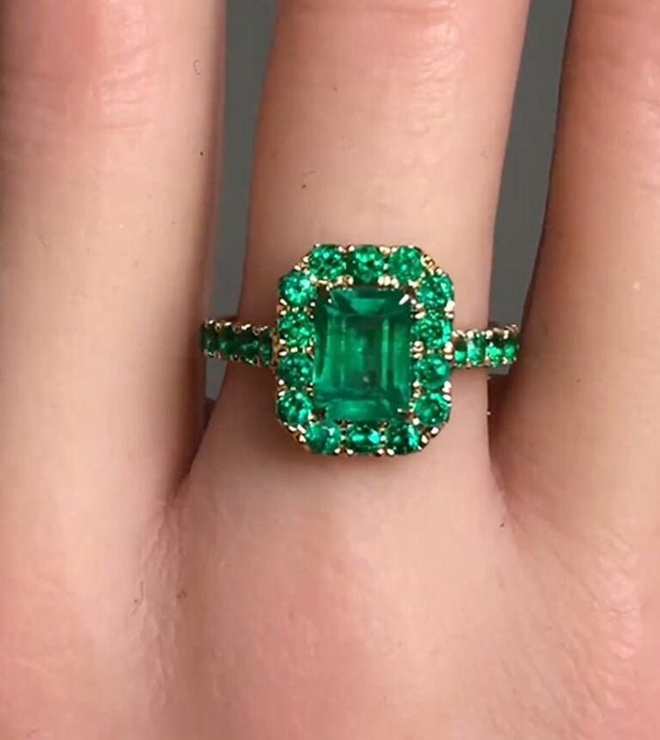 a close up of a person's hand with a green ring on their finger