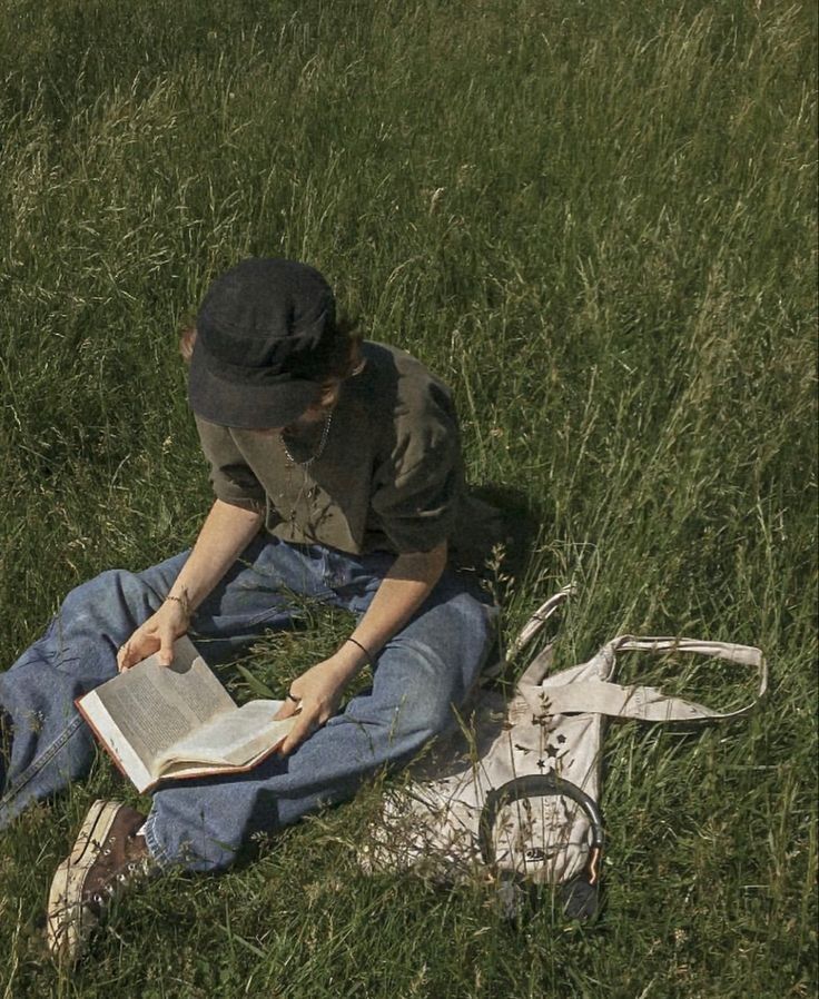 a person sitting in the grass reading a book