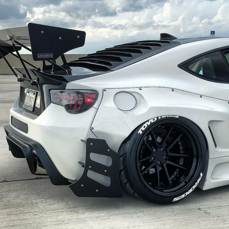 the rear end of a white sports car parked on an airport tarmac with cloudy skies in the background