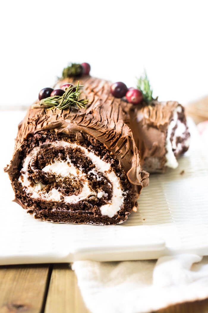 a chocolate roll with frosting and cranberries is on a white platter