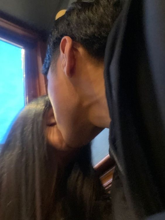 a man and woman kissing each other in front of a window with the ocean outside