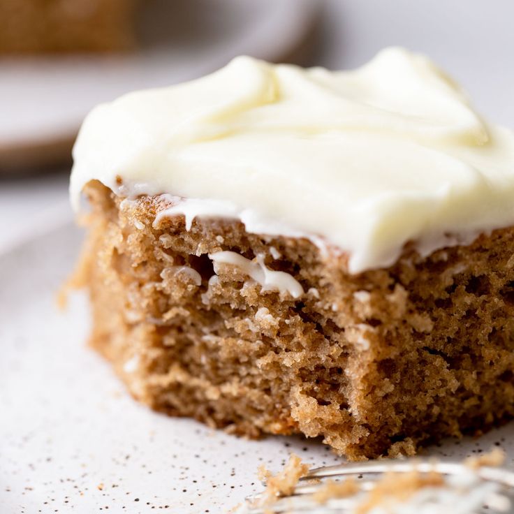 a piece of carrot cake with white frosting on a plate next to a fork