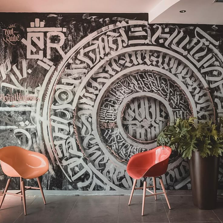 two orange chairs sitting in front of a black and white wall with writing on it