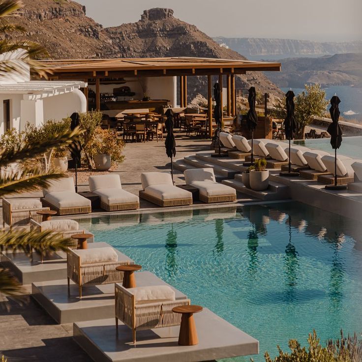 an outdoor pool with chaise lounges next to it and mountains in the background