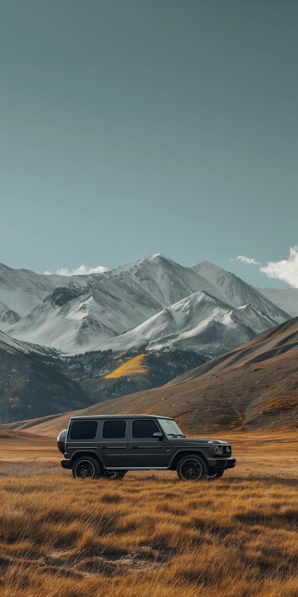 two vehicles are parked in the middle of a field with mountains in the back ground