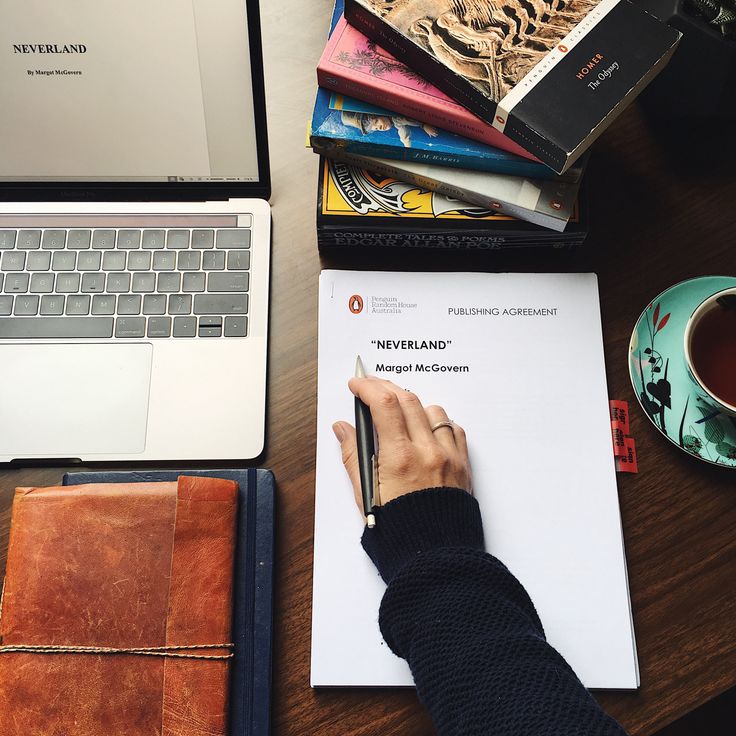 a person's hand is writing on a piece of paper next to a laptop