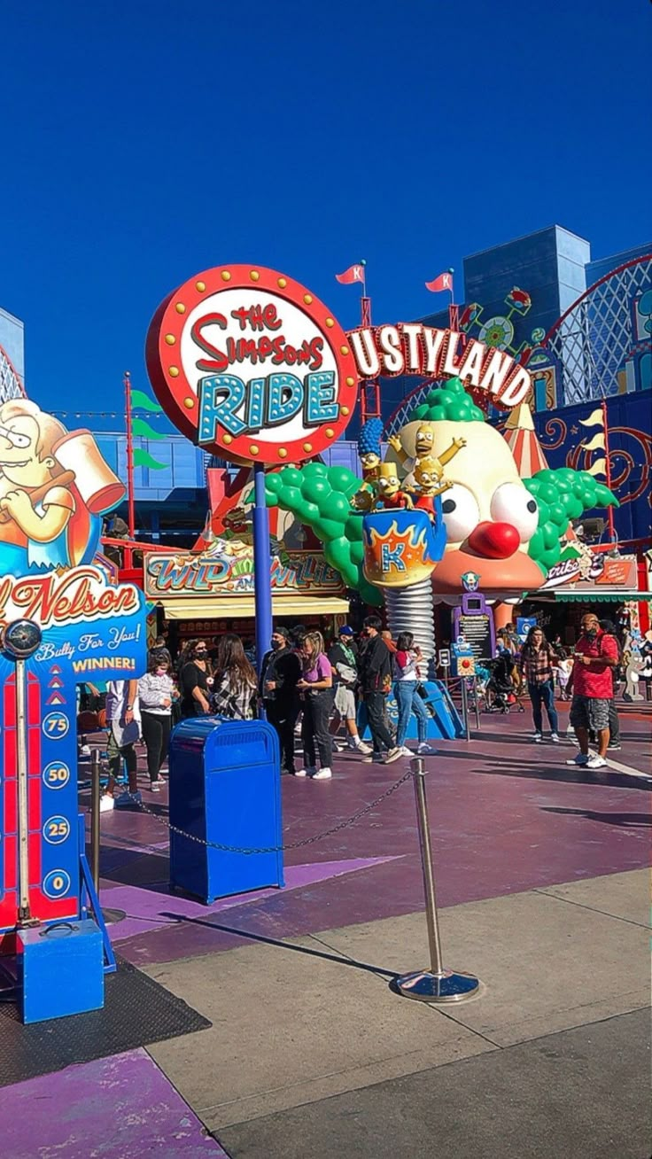 the entrance to an amusement park with many signs on it's sides and people walking around