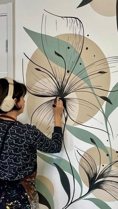 a woman with headphones on painting a flowered wallpaper design in a room