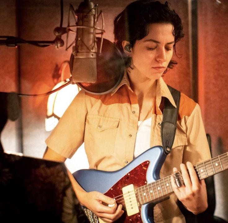 a young man playing an electric guitar in front of a microphone