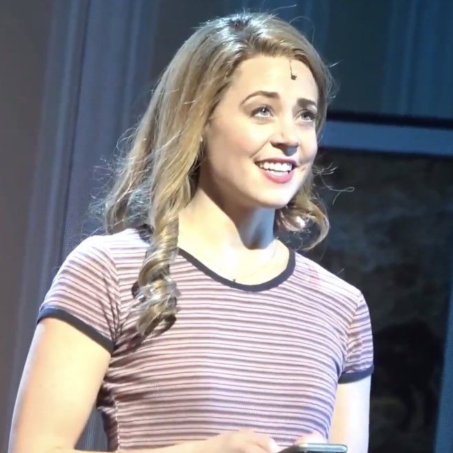 a woman standing in front of a window holding a cell phone and smiling at the camera