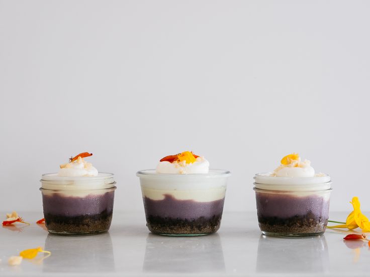 three desserts in small glass jars on a table with yellow flowers around the edges