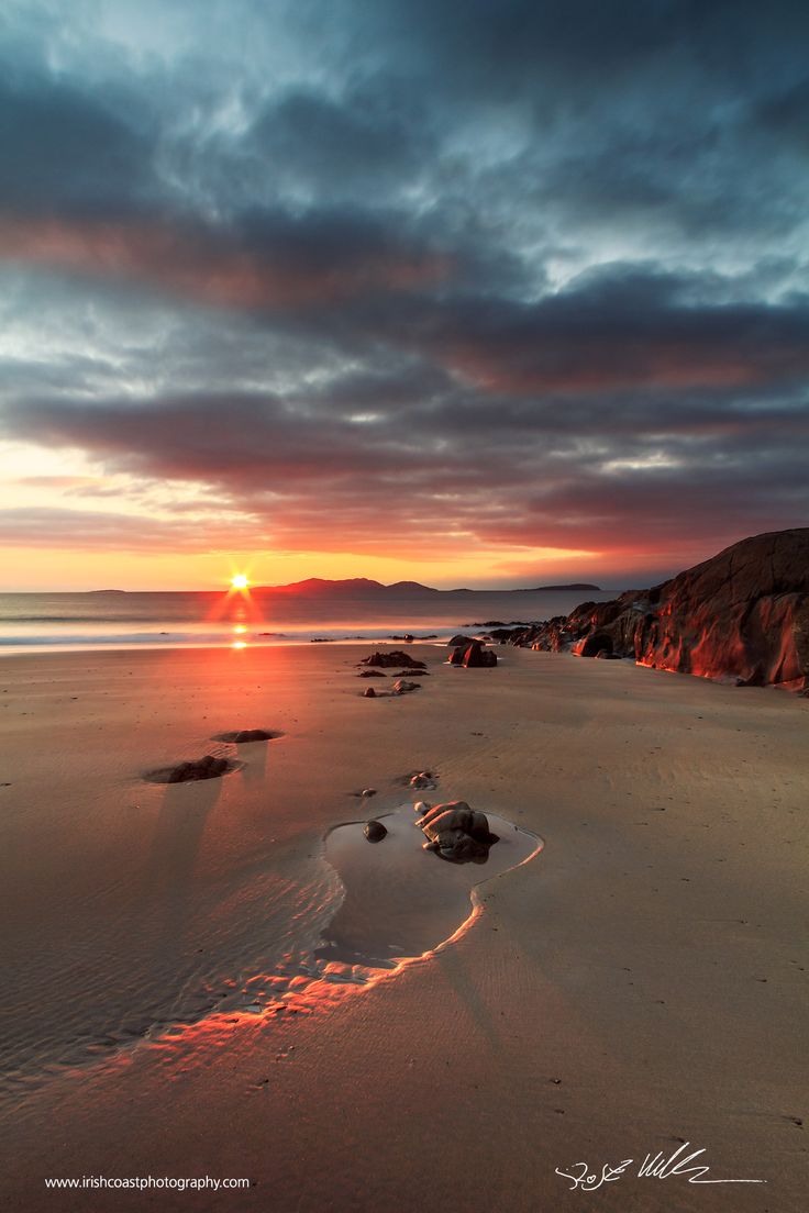 the sun is setting over some rocks on the beach