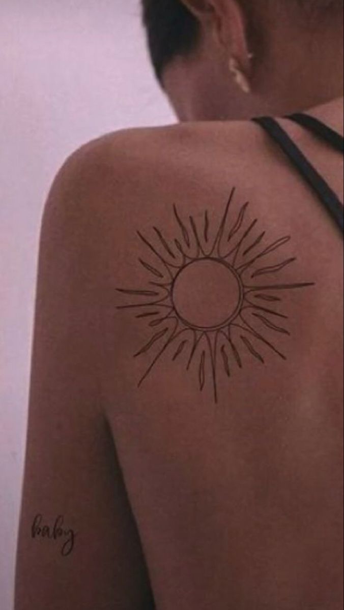 the back of a woman's shoulder with a sun tattoo on it