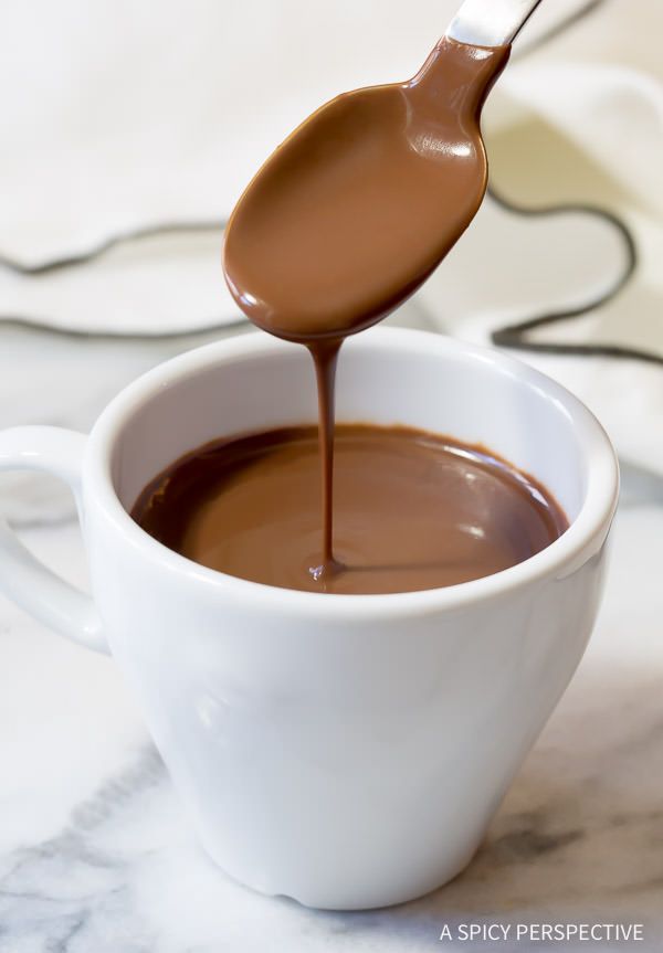 a spoon full of chocolate sauce being poured into a white cup with the liquid in it