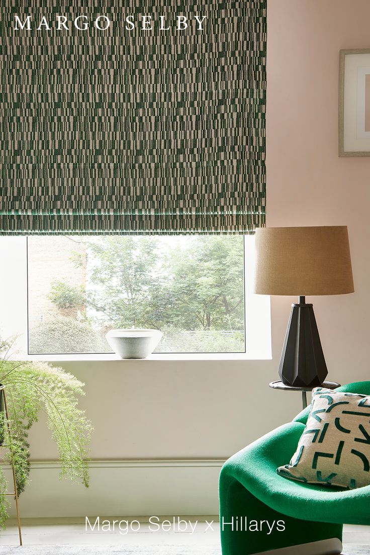 a green chair in front of a window with roman shades on it's windowsill