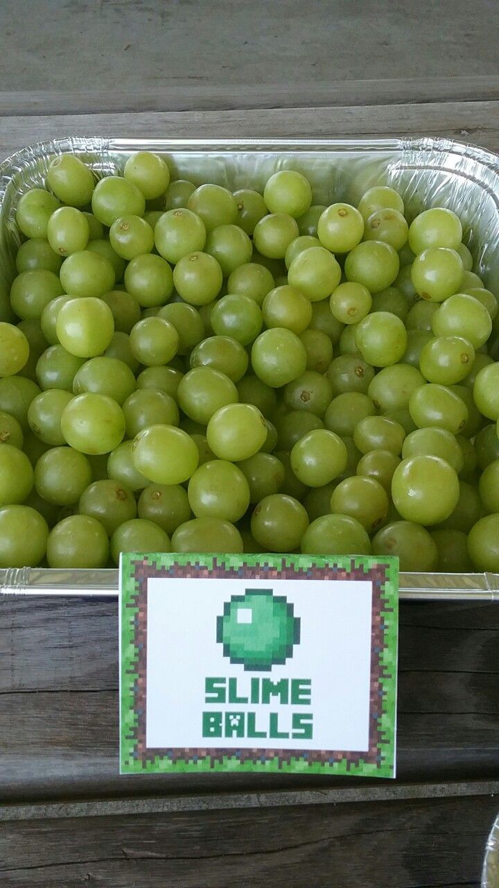 some grapes are in a plastic container on the table next to a sign that says slime balls