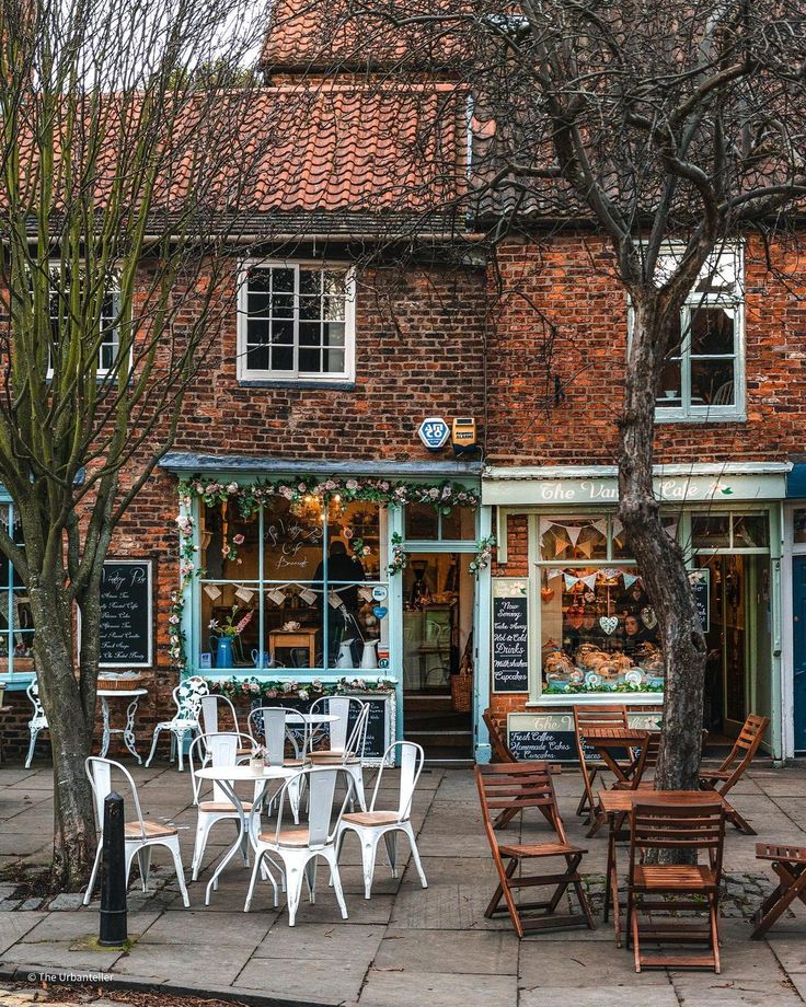 an outdoor cafe with tables and chairs in front of the storefront, surrounded by trees