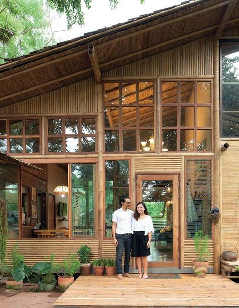 two people standing in front of a wooden house with large windows on the outside and inside