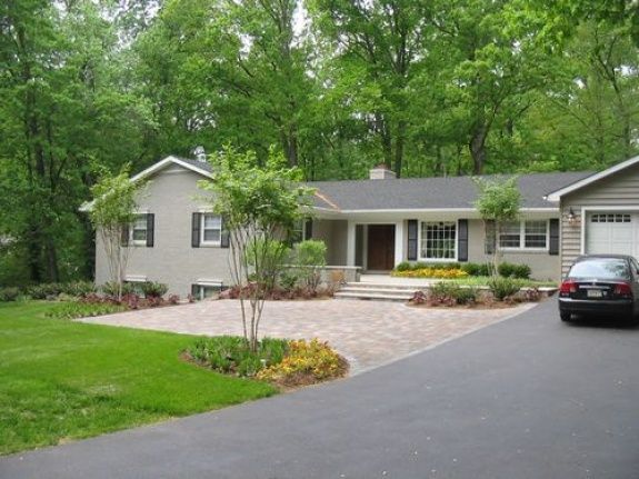 a car parked in front of a house on a driveway with trees and bushes around it