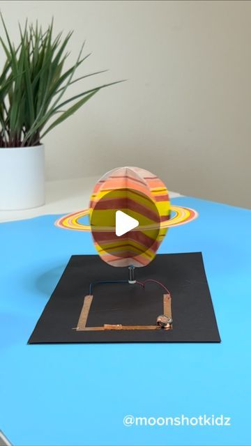 a paper model of the solar system on a table with a potted plant in the background