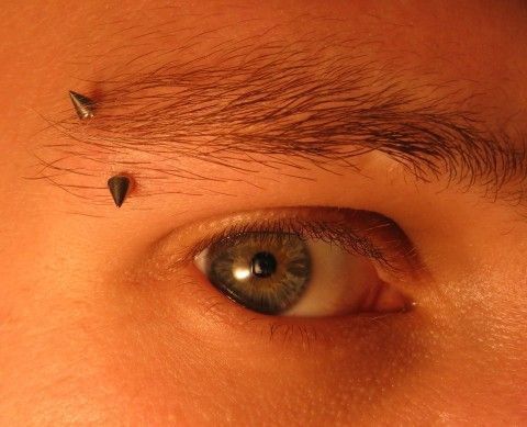 a close up of a person's eye with some piercings on their forehead