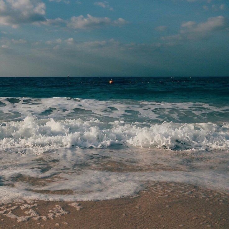 the waves are crashing on the beach and there is a sailboat in the distance