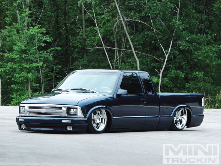 a black truck parked on top of a parking lot next to some trees and bushes