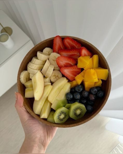 a person holding a bowl of fruit with kiwis, strawberries and bananas