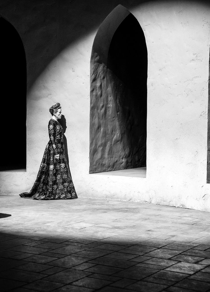 a black and white photo of a woman in a long dress standing next to an arch