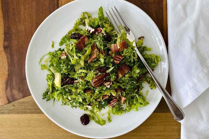 a white plate topped with lettuce and cranberries next to a fork