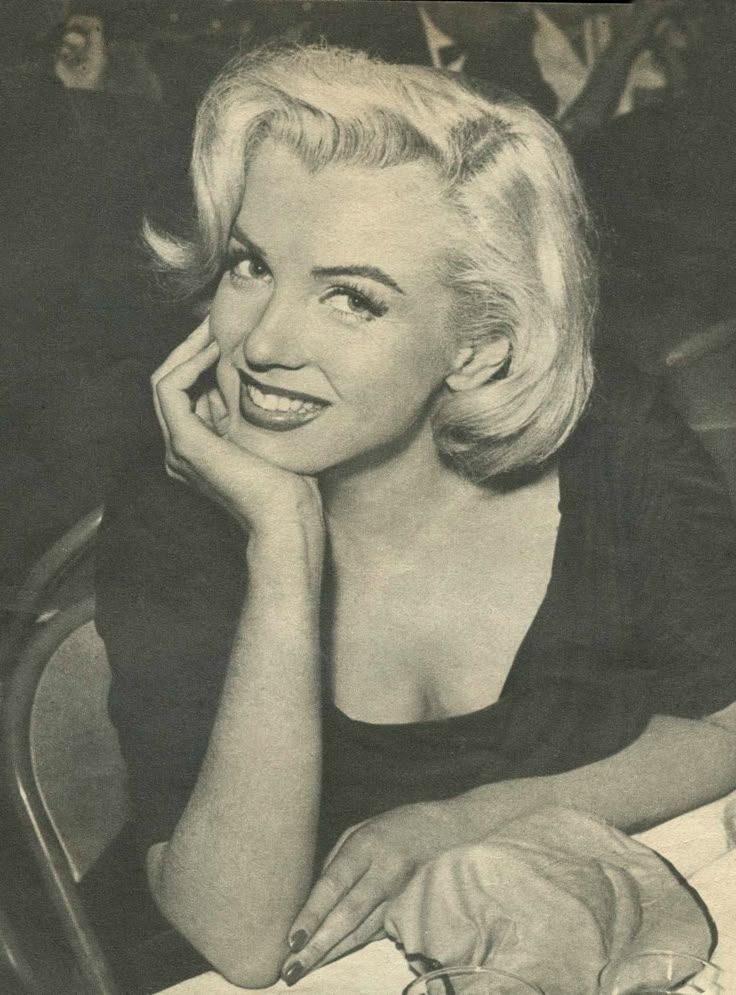 an old black and white photo of a woman sitting at a table with her hand on her face