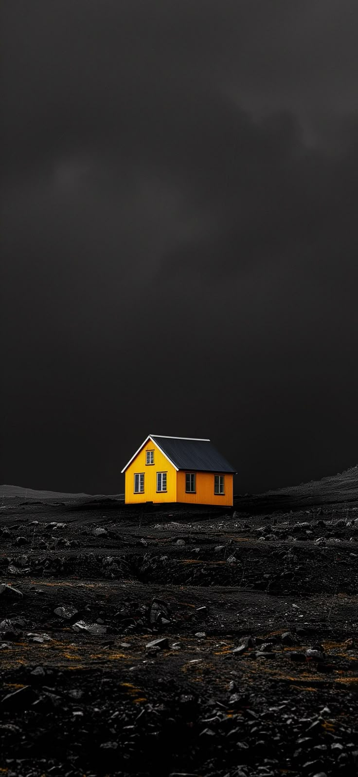 a yellow house sitting on top of a black field under a dark sky with clouds