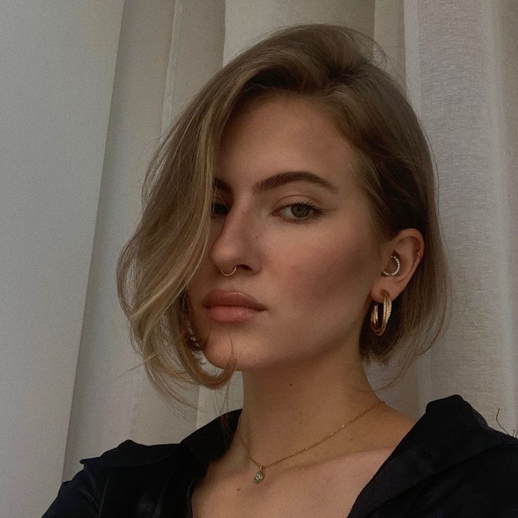 a woman with blonde hair wearing gold hoop earrings and a black top is looking off to the side