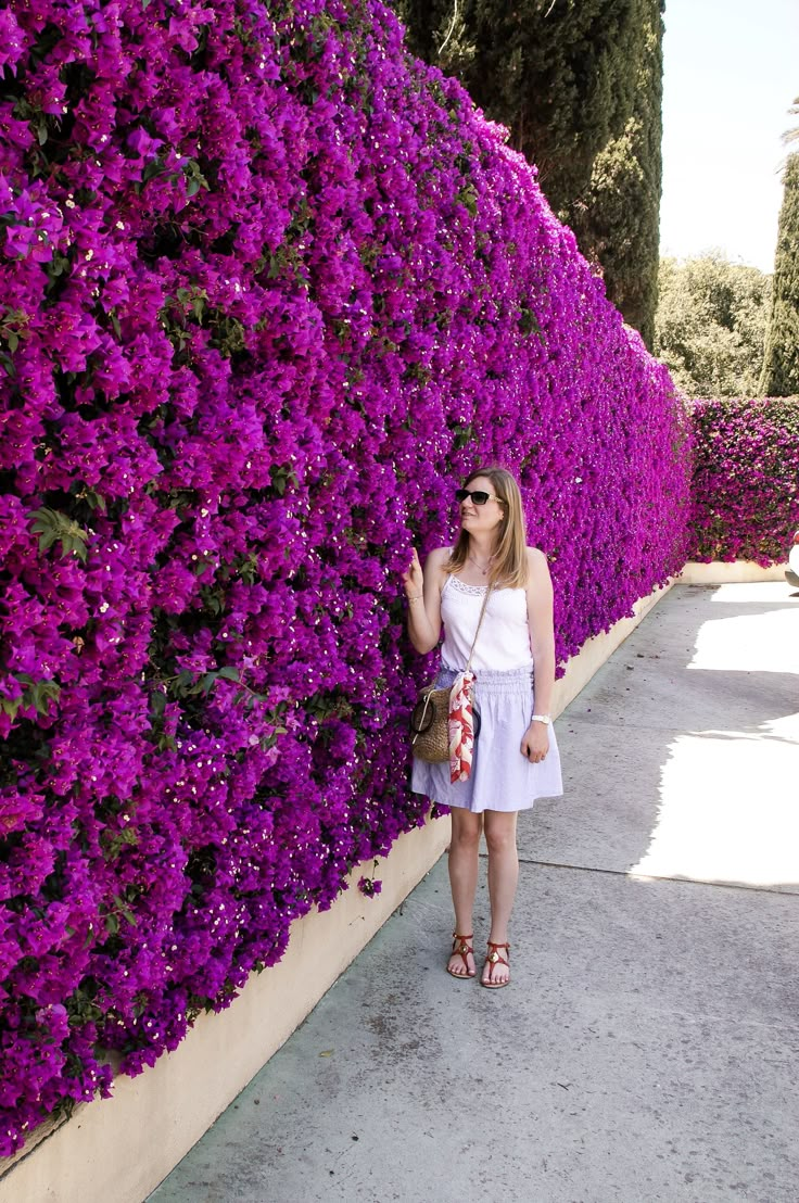 a woman standing in front of a purple flower wall with her hand on her hip