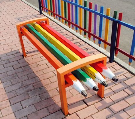 a bench made out of colored pencils sitting on the side of a road next to a colorful fence