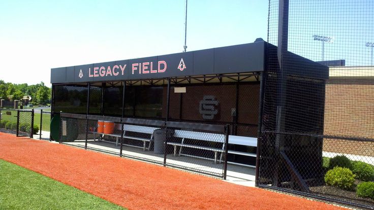 an empty baseball field with benches on the grass and fenced in area next to it