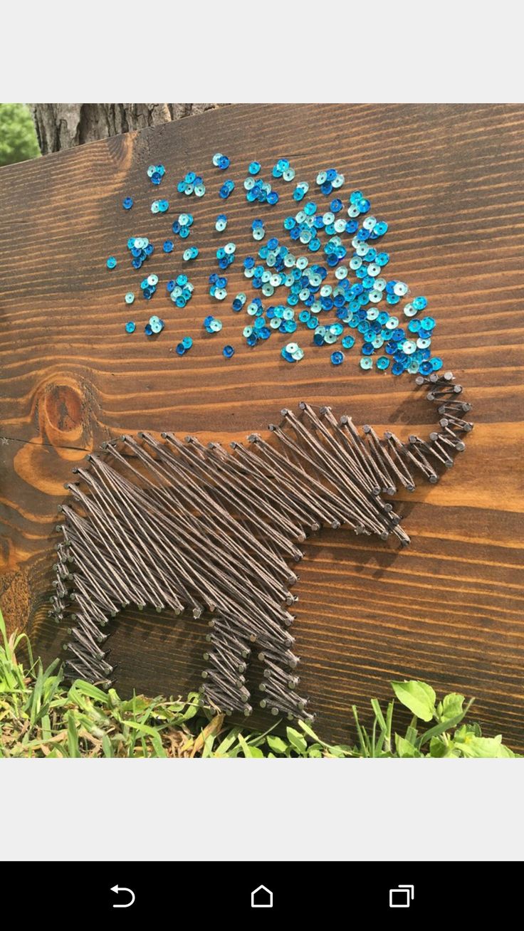 a dog made out of wire and blue beads on a wooden sign in the grass