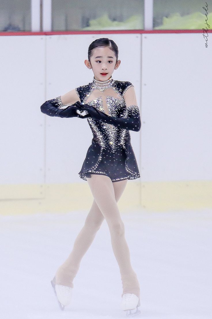 a woman in a black and silver dress skating on an ice rink with her arms outstretched